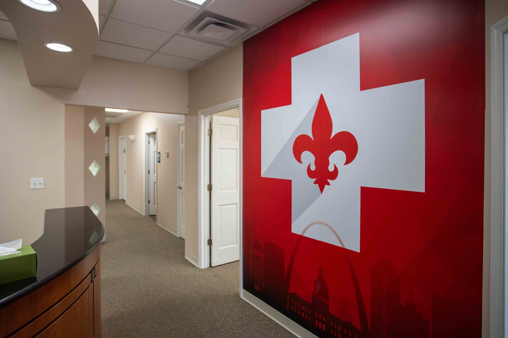 Hallway with a large red wall featuring the STL Urgent Dental logo: a white cross and fleur-de-lis.