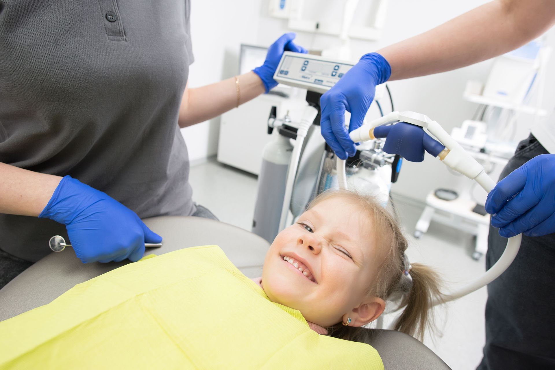 Dentist treating a smiling child in a bright dental clinic, with gloved hands and dental tools visible