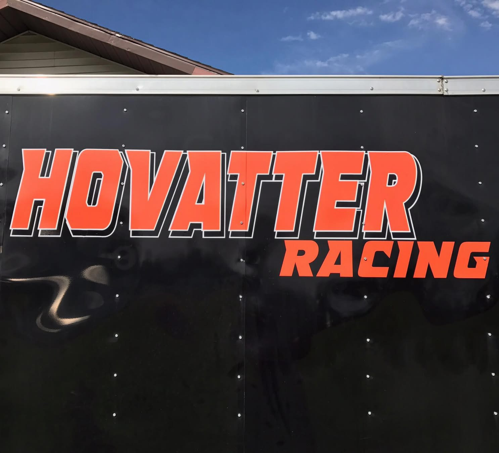 Black trailer side with orange “HOVATTER RACING” lettering and a partial roofline visible above