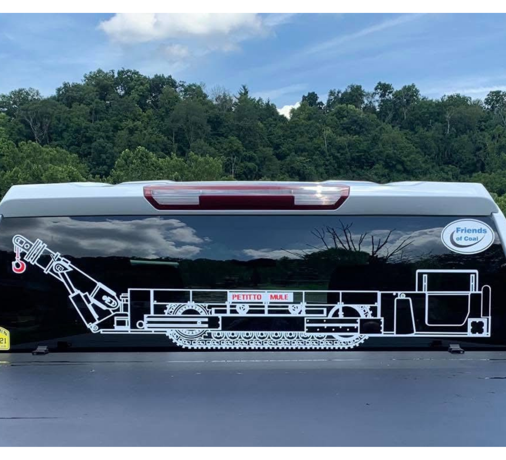 White trailer with a black side panel featuring a line-art train mural, parked outdoors by trees.