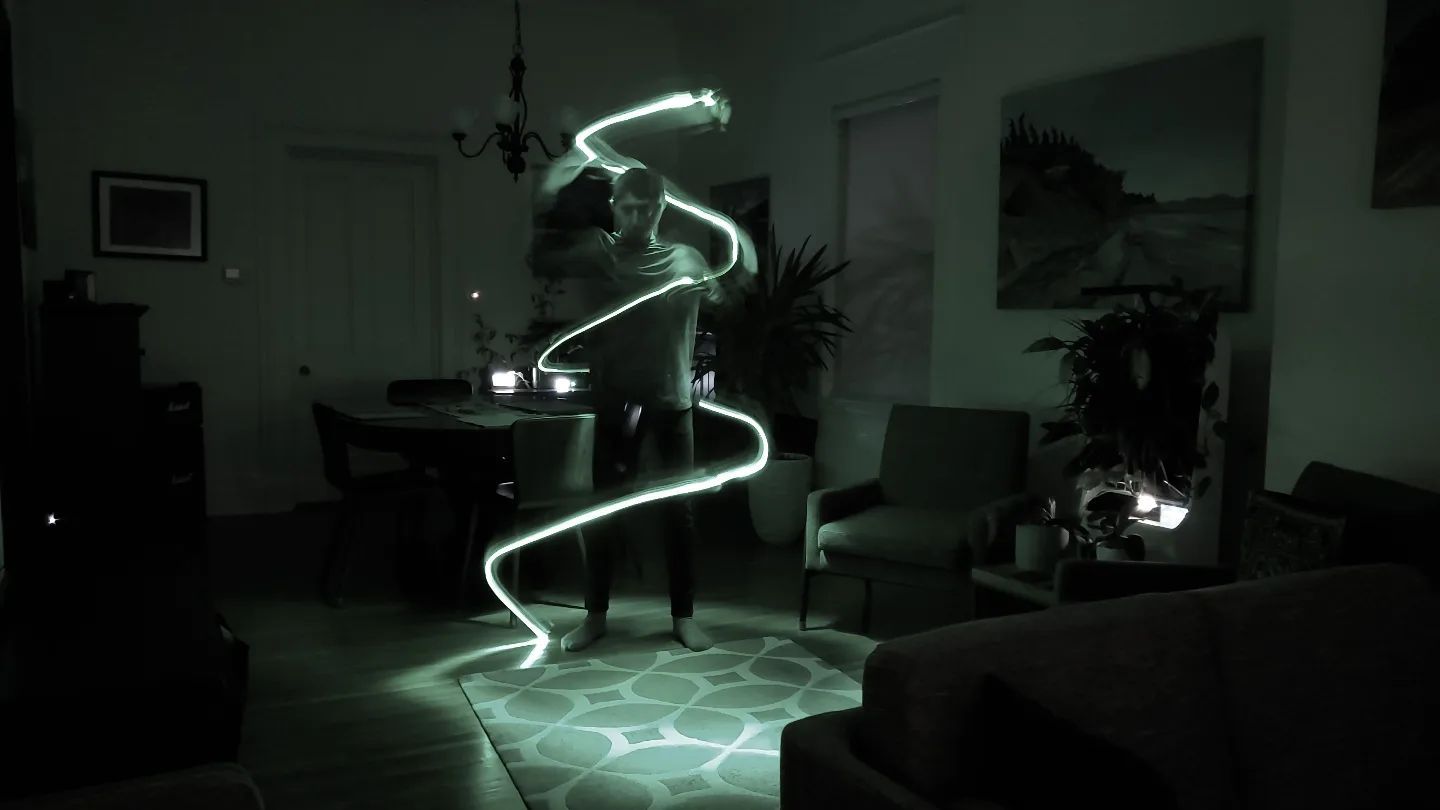 Person in a room, light painting with a glowing white line around them in a long exposure.