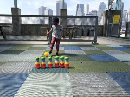 A young boy is playing a game of bocce ball on a rooftop with a city skyline in the background.