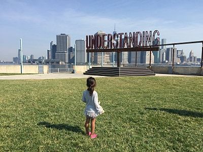 A little girl is standing in the grass in front of a sign that says understanding.