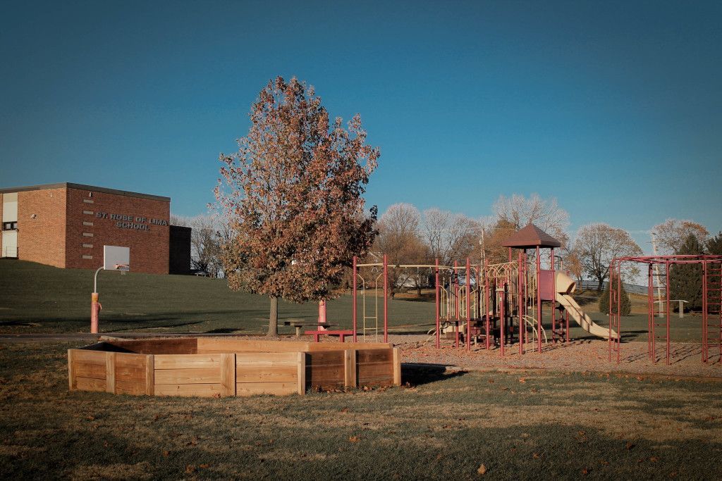 A playground in a park with a brick building in the background.