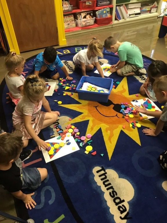 A group of children are sitting on a rug that says thursday