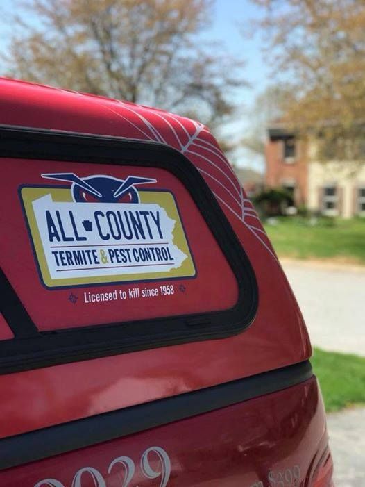 A red vehicle displays a yellow logo for All-County Termite & Pest Control, parked in front of a house on a sunny day.