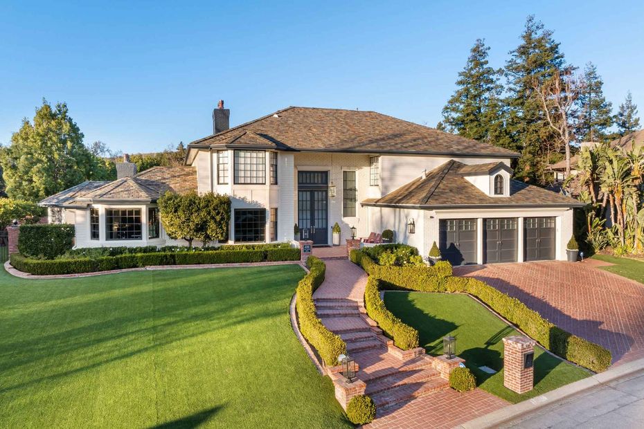 Large two-story suburban house with a manicured lawn, curved walkway, and landscaped front yard