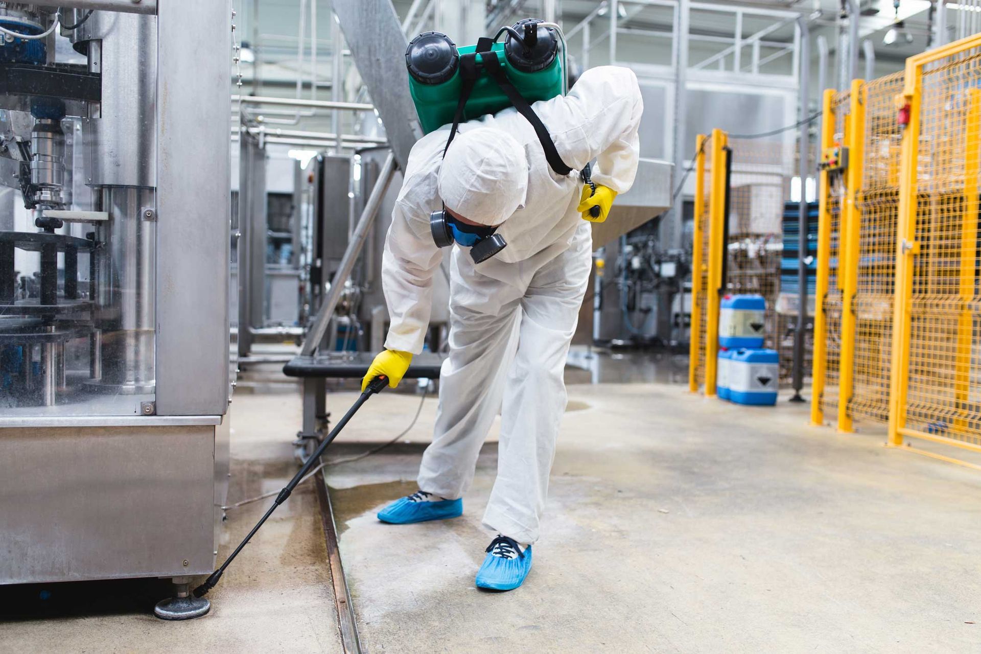 Worker in white protective suit cleaning industrial floor with a pressure washer in a factory. Worker in white protective suit cleaning industrial floor with a pressure washer in a factory.