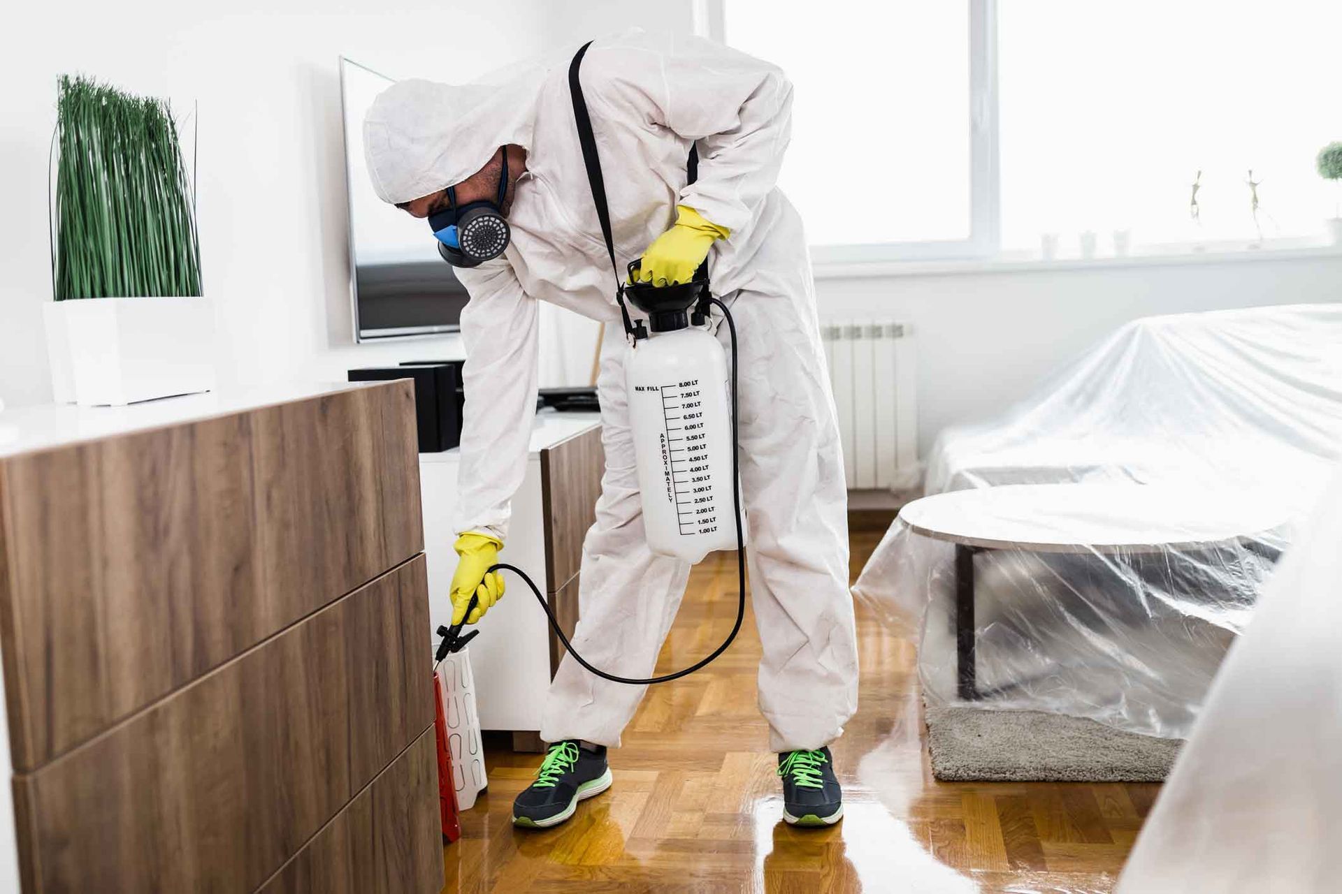 Worker in white protective suit spraying disinfectant in a home living room Worker in white protective suit spraying disinfectant in a home living room