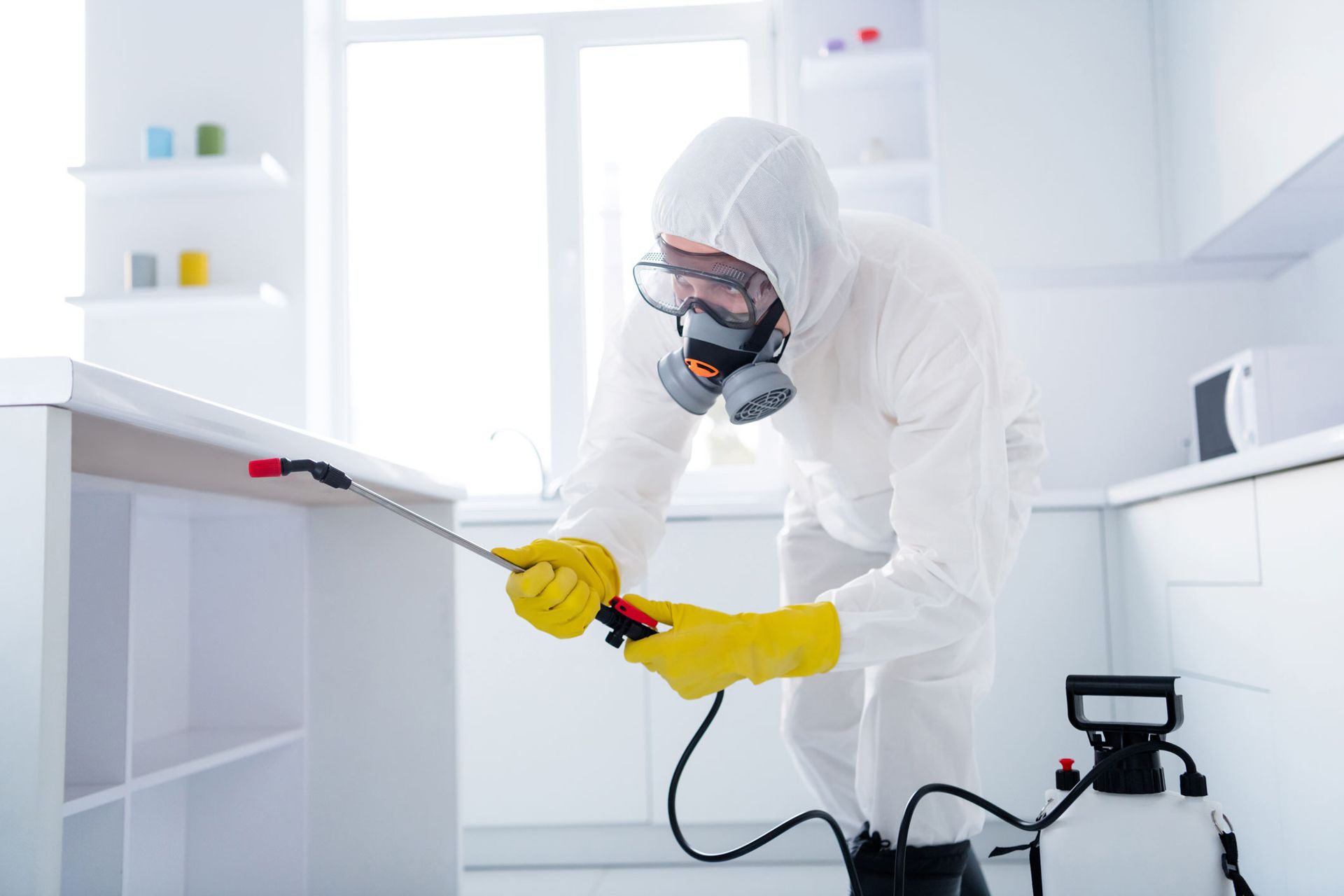 Person in white hazmat suit spraying disinfectant in a bright kitchen Person in white hazmat suit spraying disinfectant in a bright kitchen