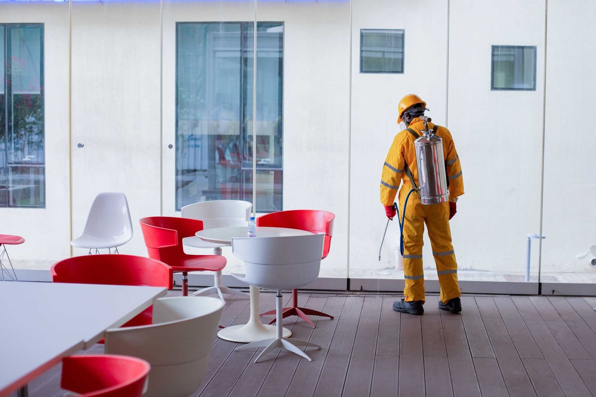 Worker in yellow safety gear stands in a modern office lounge with red chairs and white tables. Worker in yellow safety gear stands in a modern office lounge with red chairs and white tables.