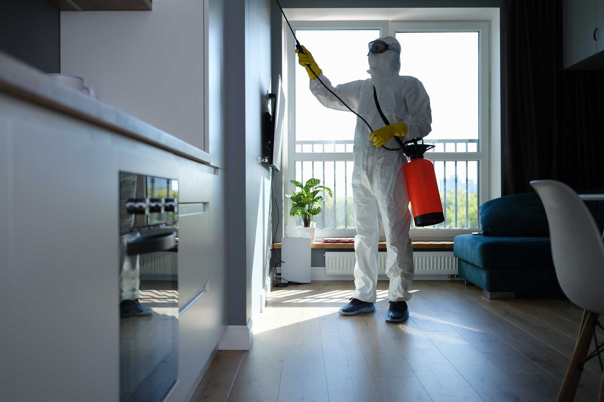 Person in white protective suit spraying disinfectant in a modern living room near a window