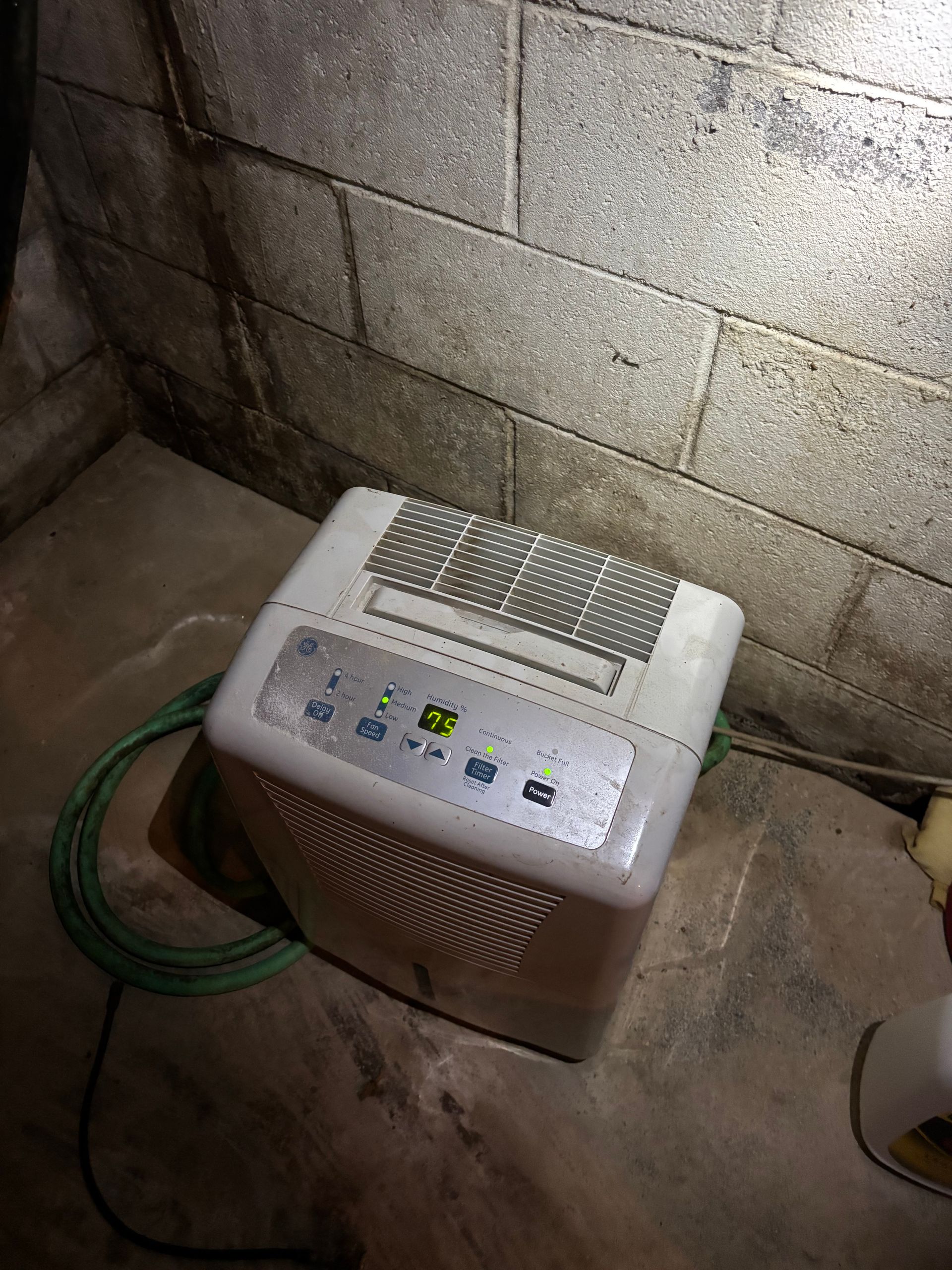 Small white and brown dehumidifier on a concrete floor beside a cinderblock wall, with a green hose nearby | Termite Treatment | Lancaster, PA Small white and brown dehumidifier on a concrete floor beside a cinderblock wall, with a green hose nearby | Termite Treatment | Lancaster, PA