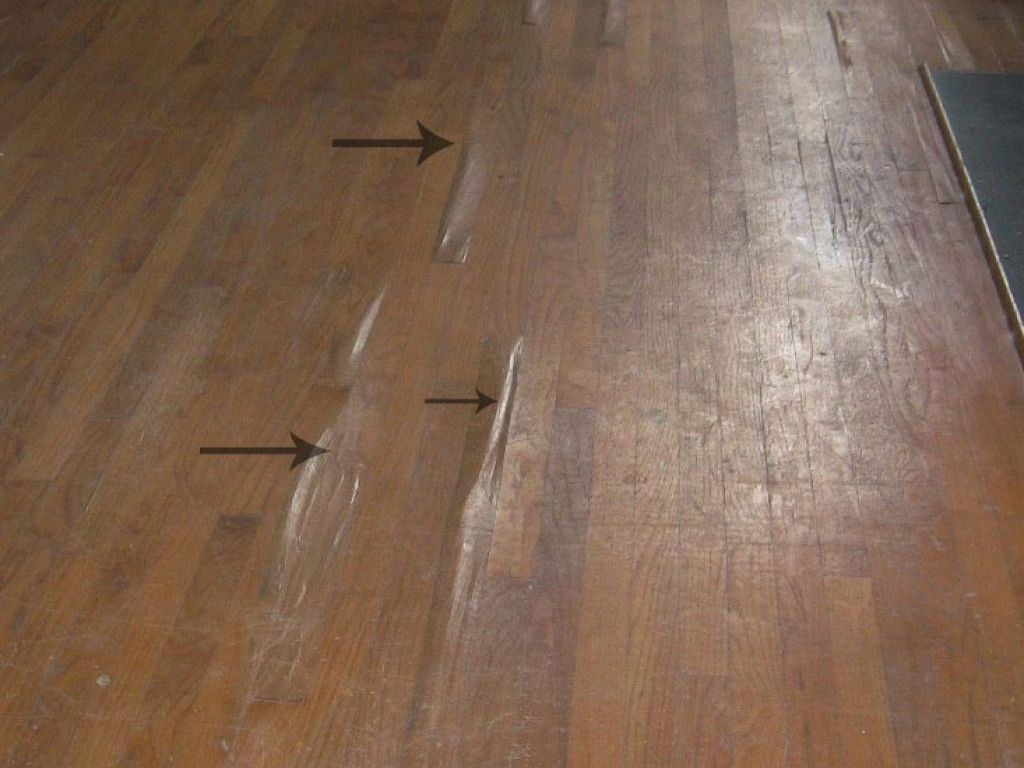 Hardwood flooring showing three raised, buckled planks highlighted by black arrows indicating damage.