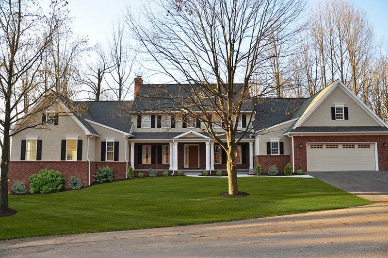A large two-story suburban house with a brick and light-colored siding facade, a double garage, and a front lawn.