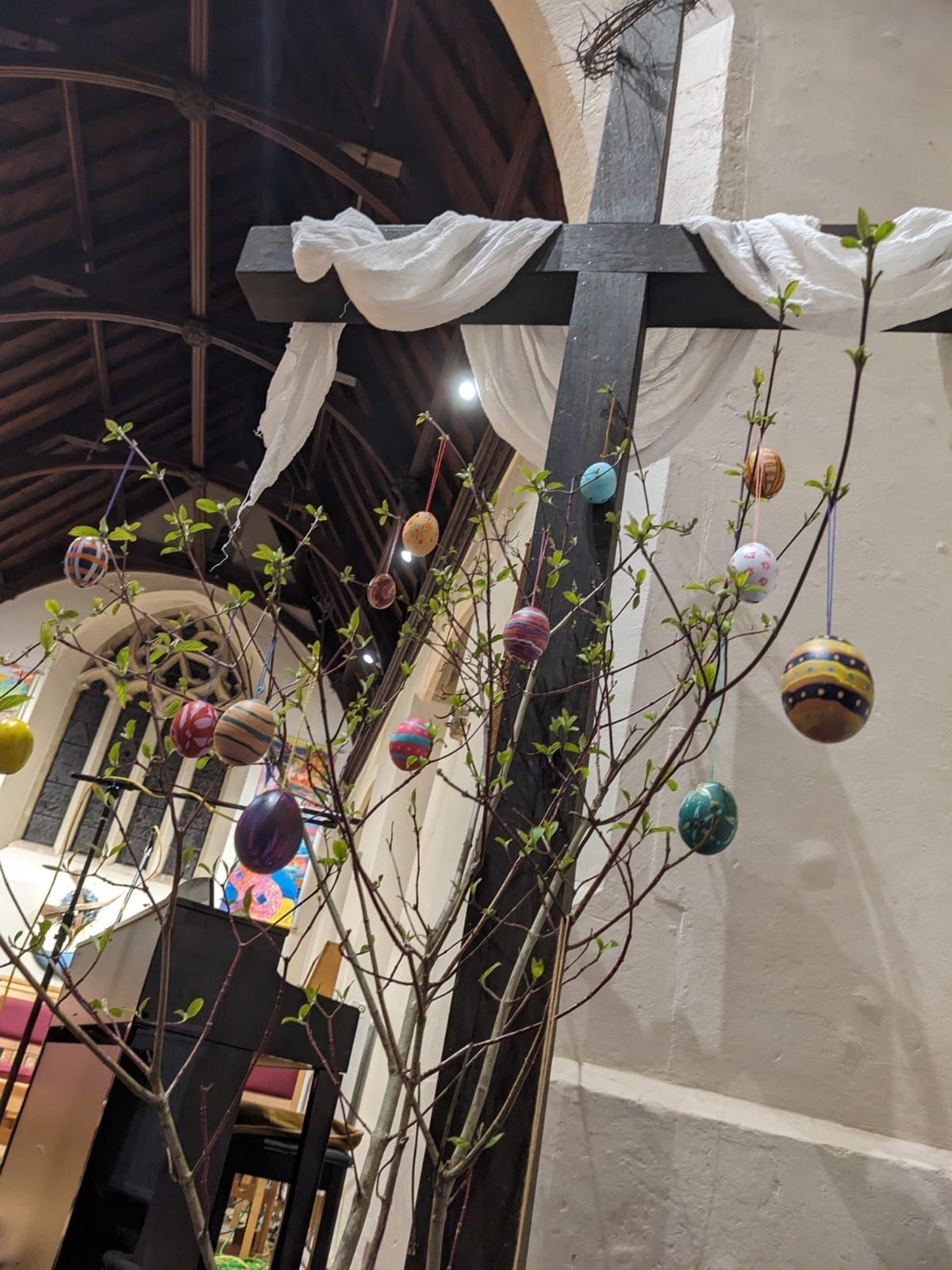 Easter decorations in church: a dark wooden cross with hanging painted eggs and budding branches.