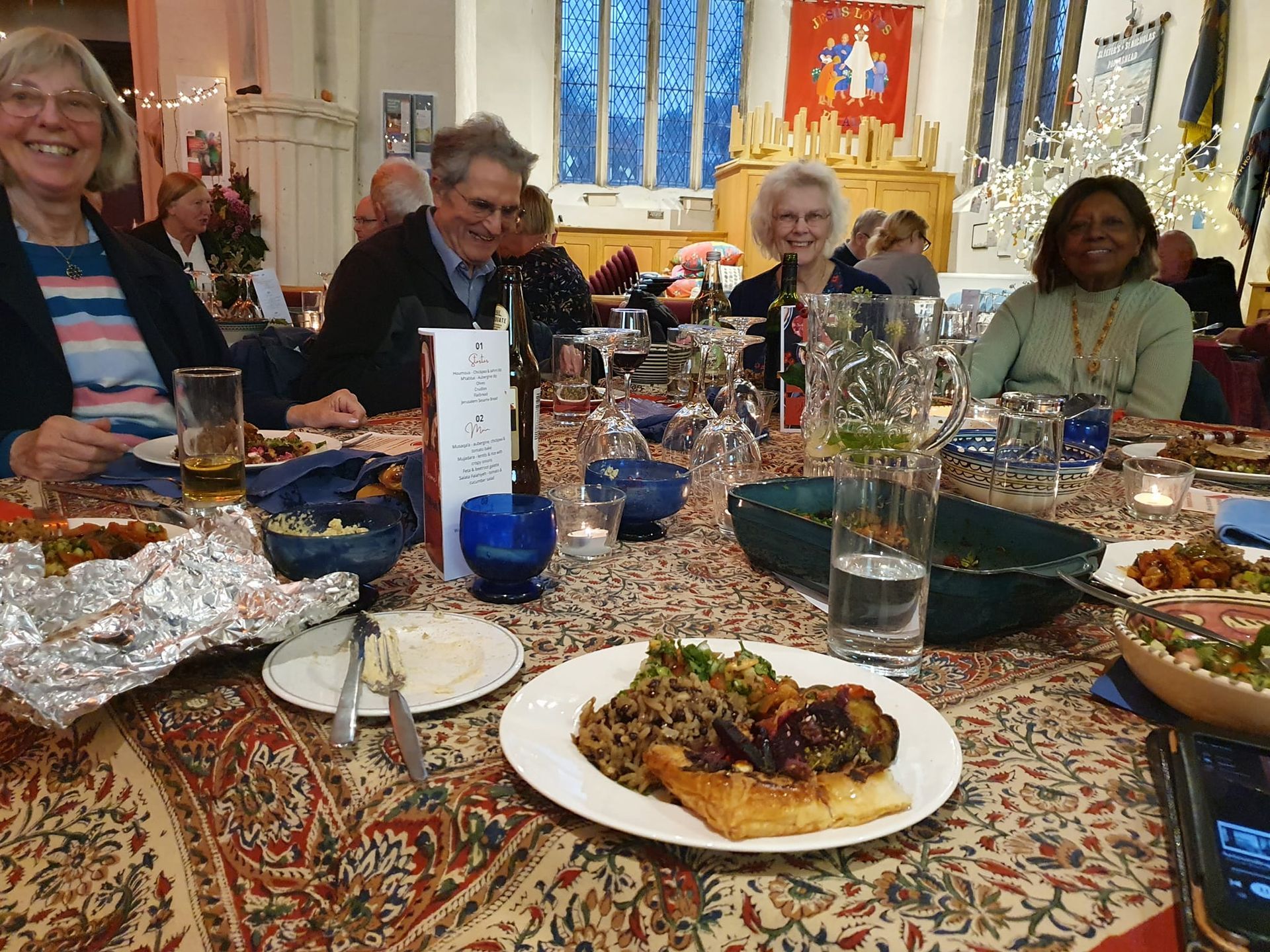 People seated around a table, enjoying a meal. Various food dishes and drinks are present.
