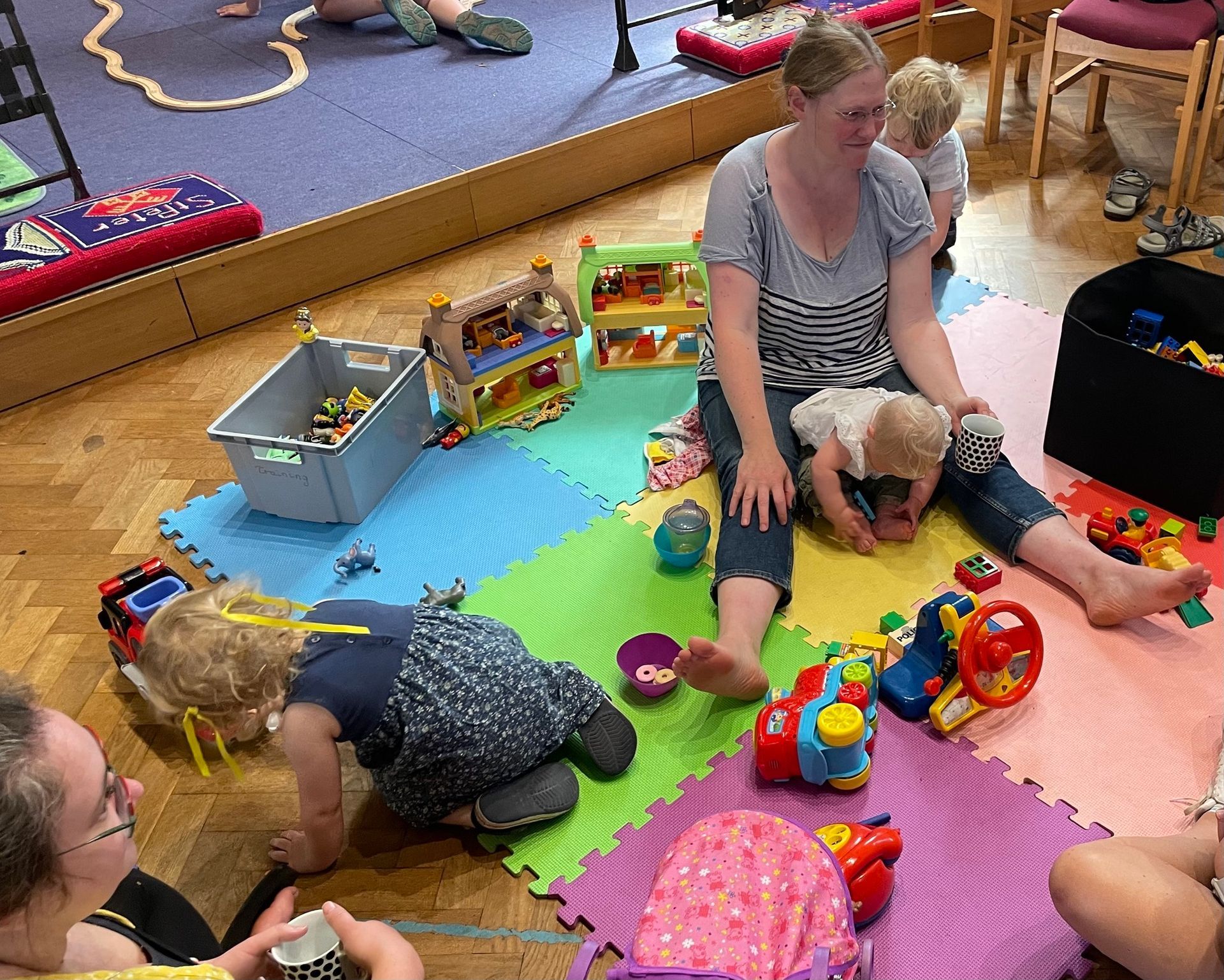 Children and adult playing on mats with toys in a room.