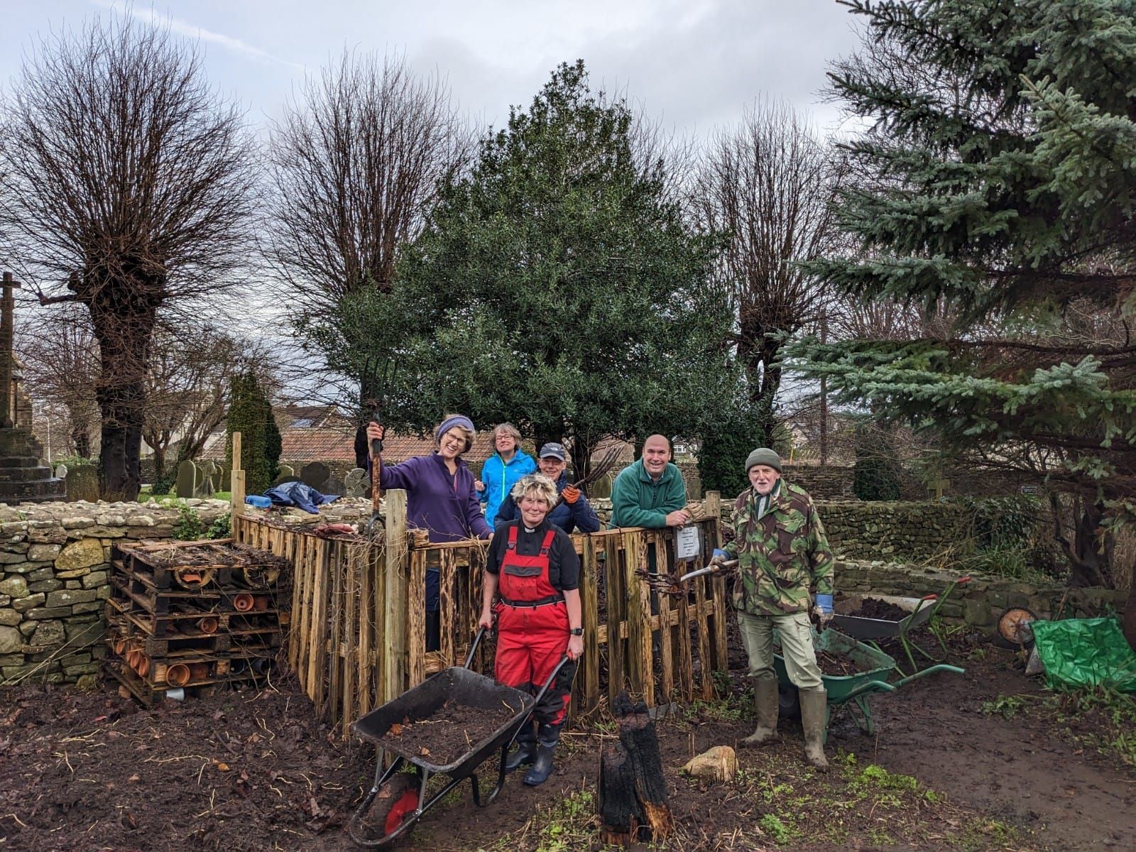 Group of people working at a compost bin in an outdoor setting on a cloudy day.
