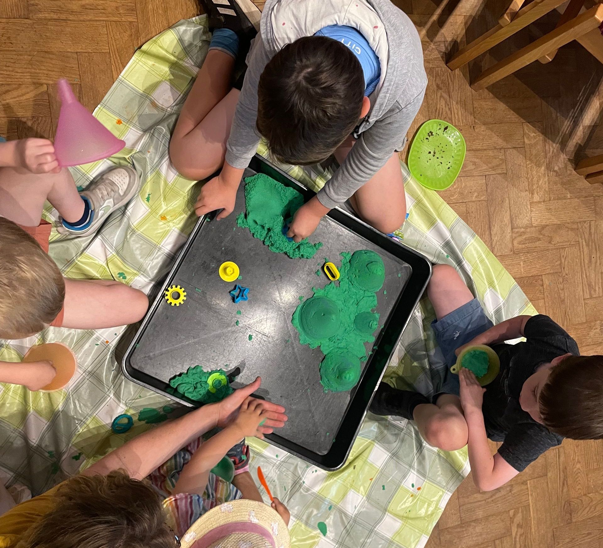 Children playing with green sand in a tray on a patterned mat.