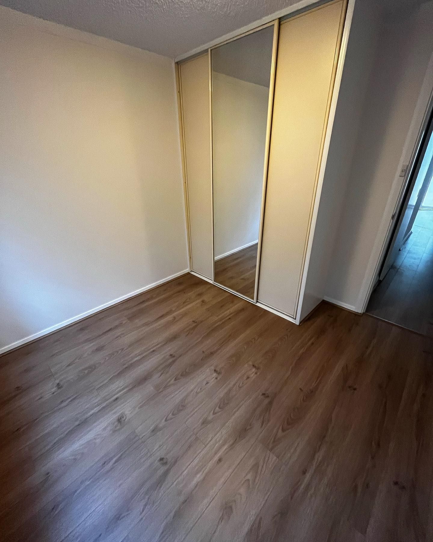 A bedroom with hardwood floors and sliding mirrored doors.