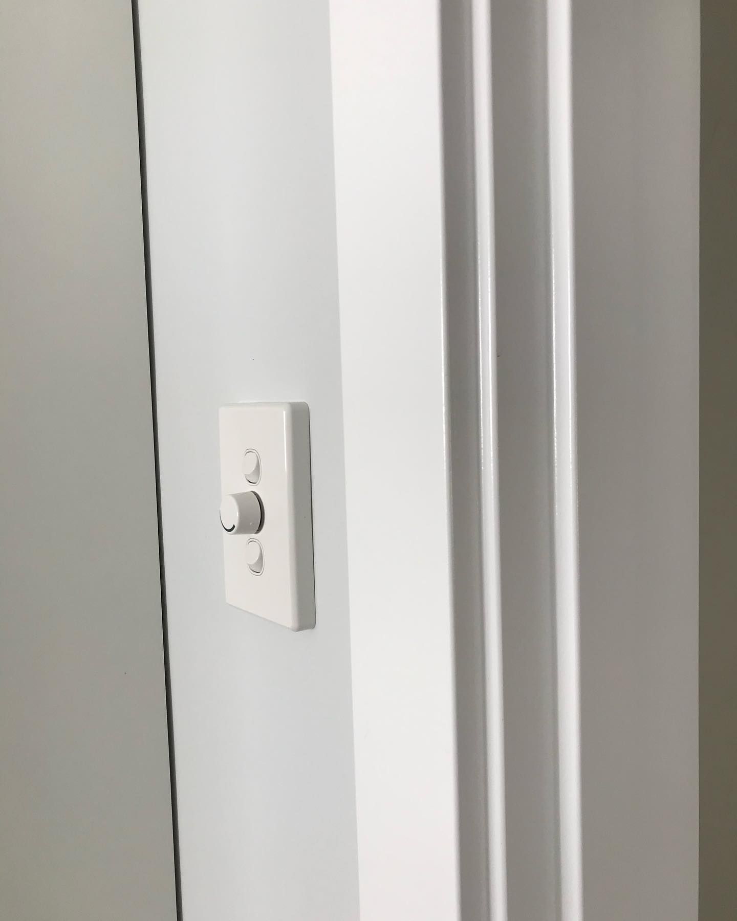 A white light switch on a white wall next to a door.