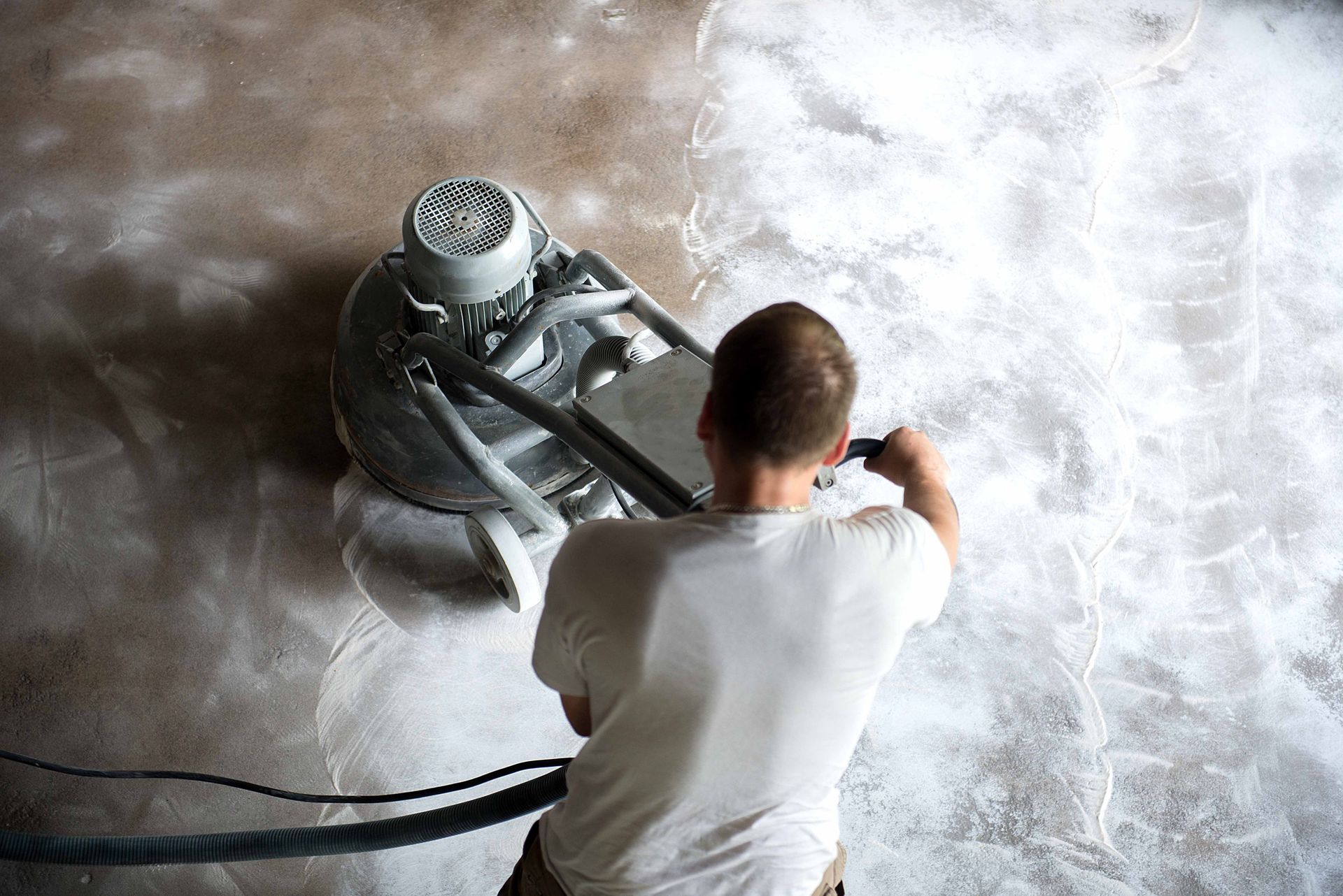 A worker in a family home living room grinding a concrete surface before applying epoxy flooring. A worker in a family home living room grinding a concrete surface before applying epoxy flooring.