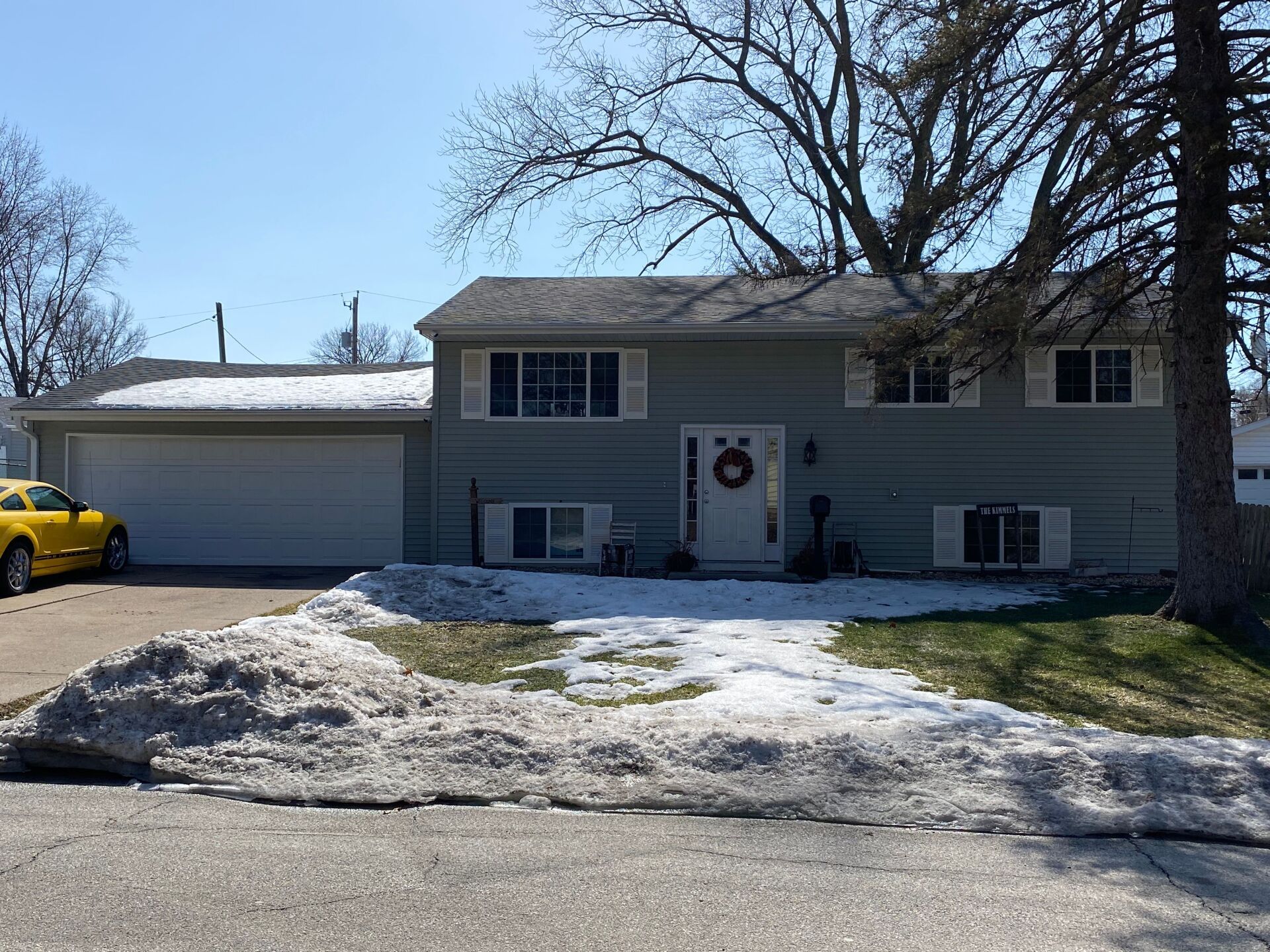 A yellow car is parked in front of a house with snow on the ground.