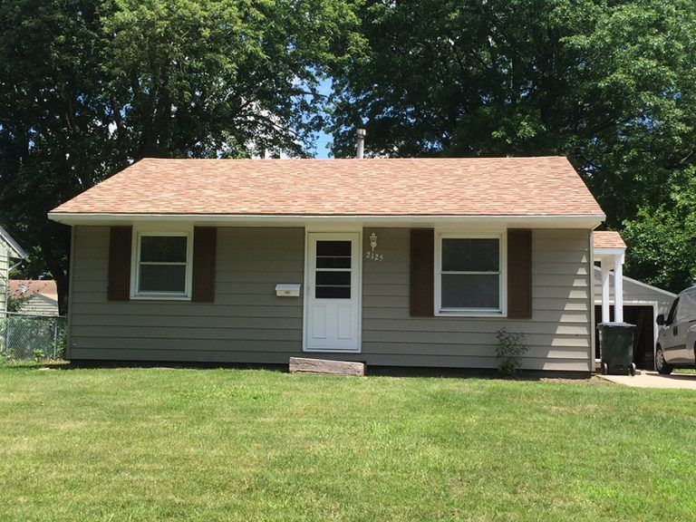 A small house with a brown roof and brown shutters is sitting on top of a lush green lawn.
