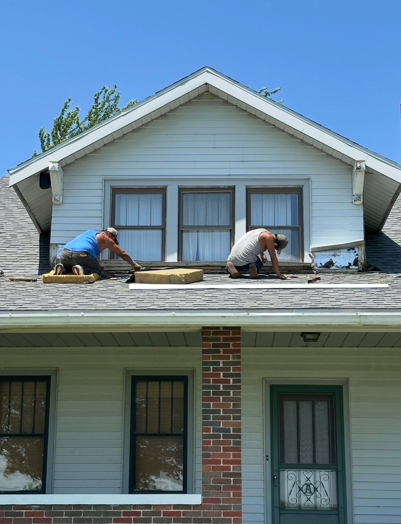 Two men are working on a roof with hammers and nails.
