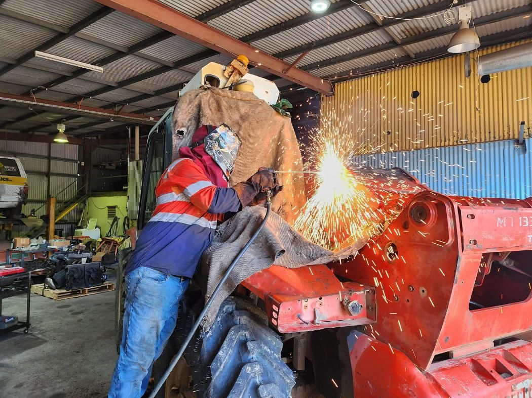 Skilled Welder Is Welding A Red Tractor Parked In A Garage — Rowdraulics NQ Pty Ltd in Cairns, QLD