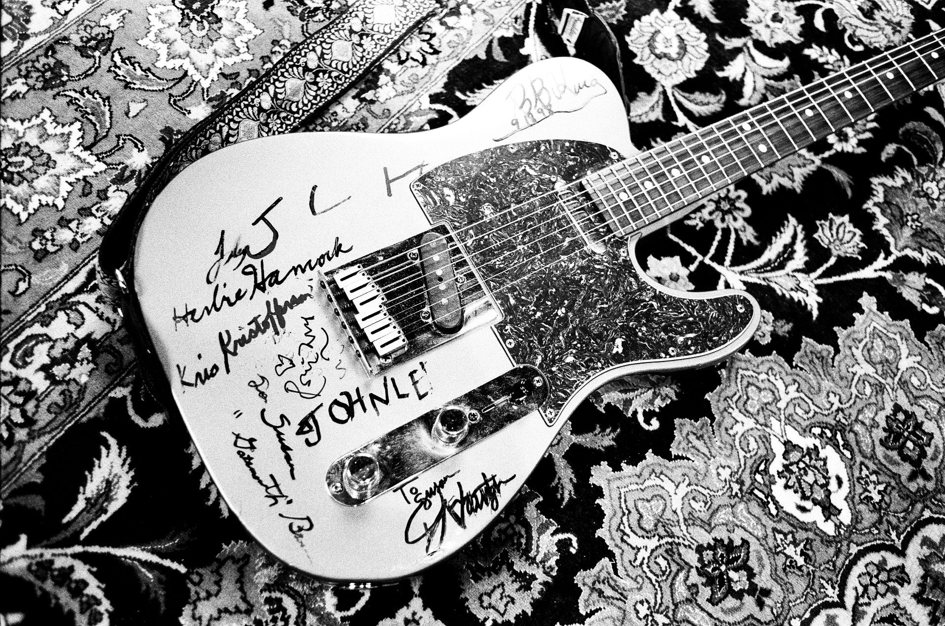 A guitar is laying on a rug with signatures on it