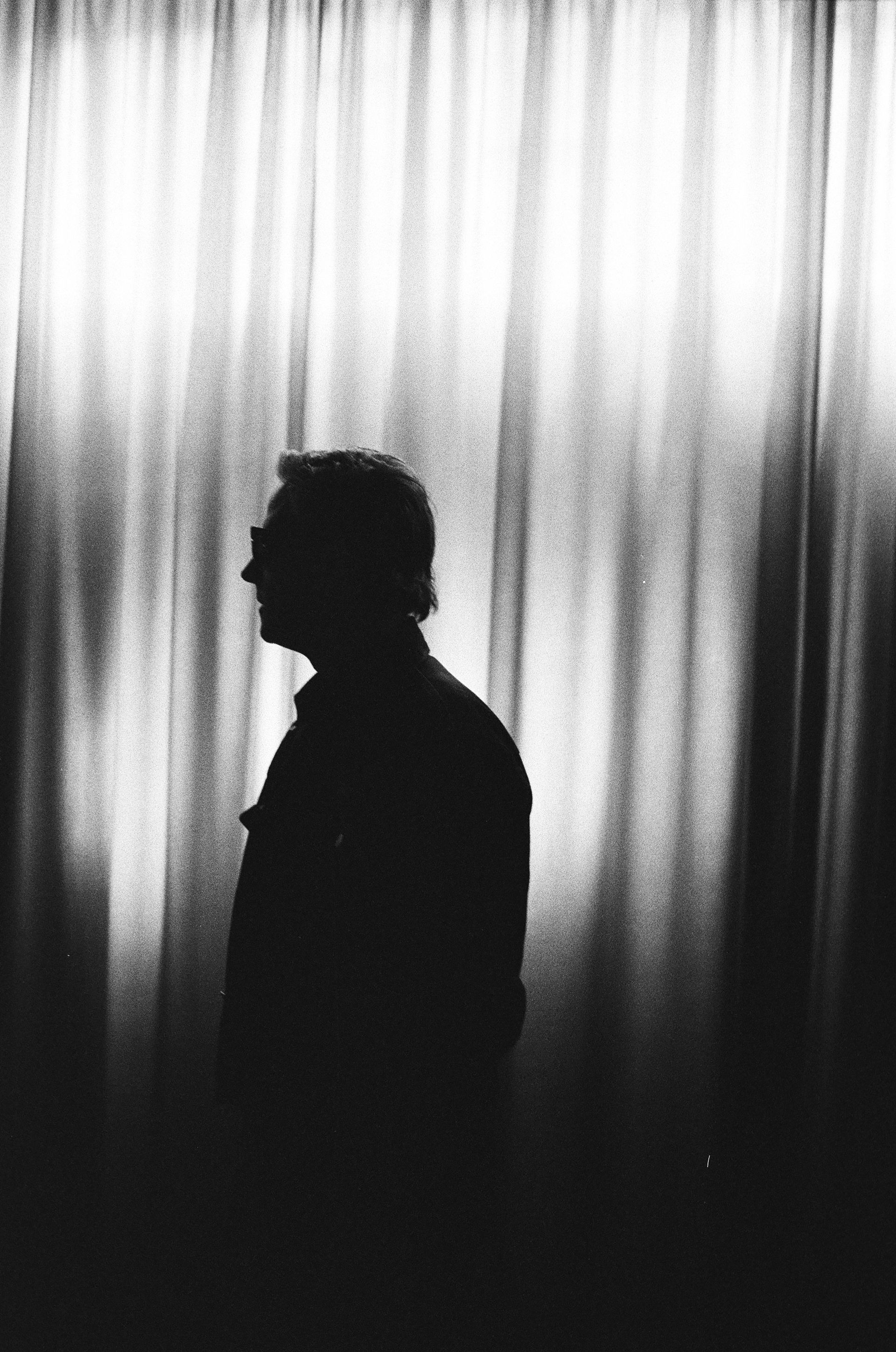 A silhouette of a man standing in front of a window with curtains.