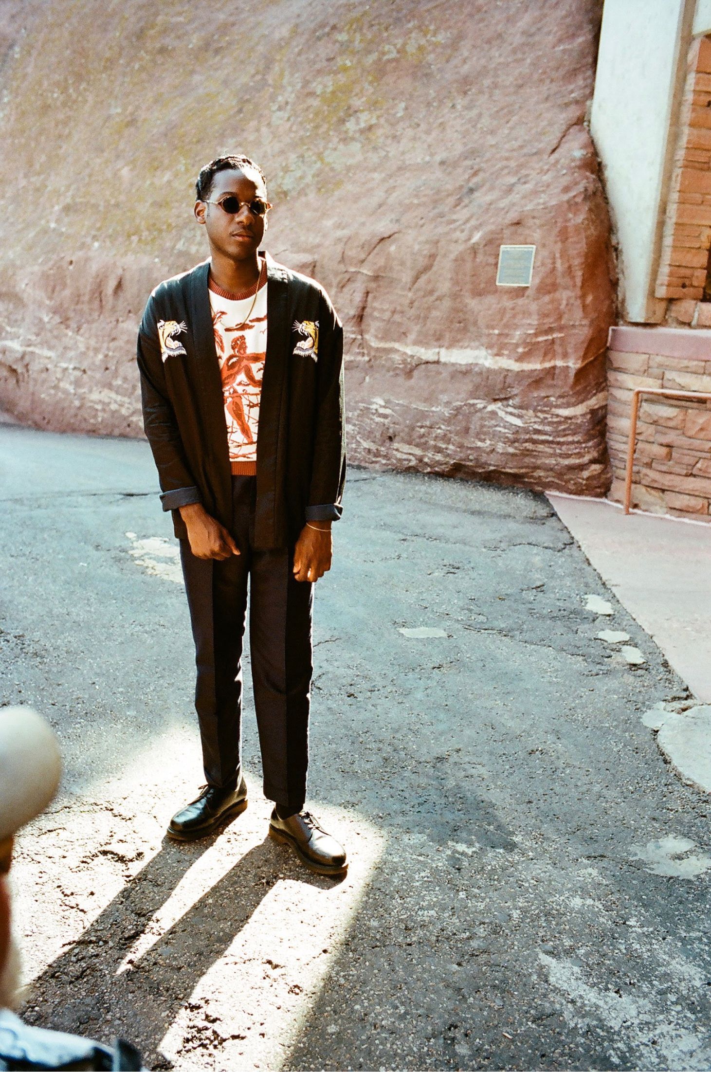 A man in a suit and sunglasses is standing on a street.