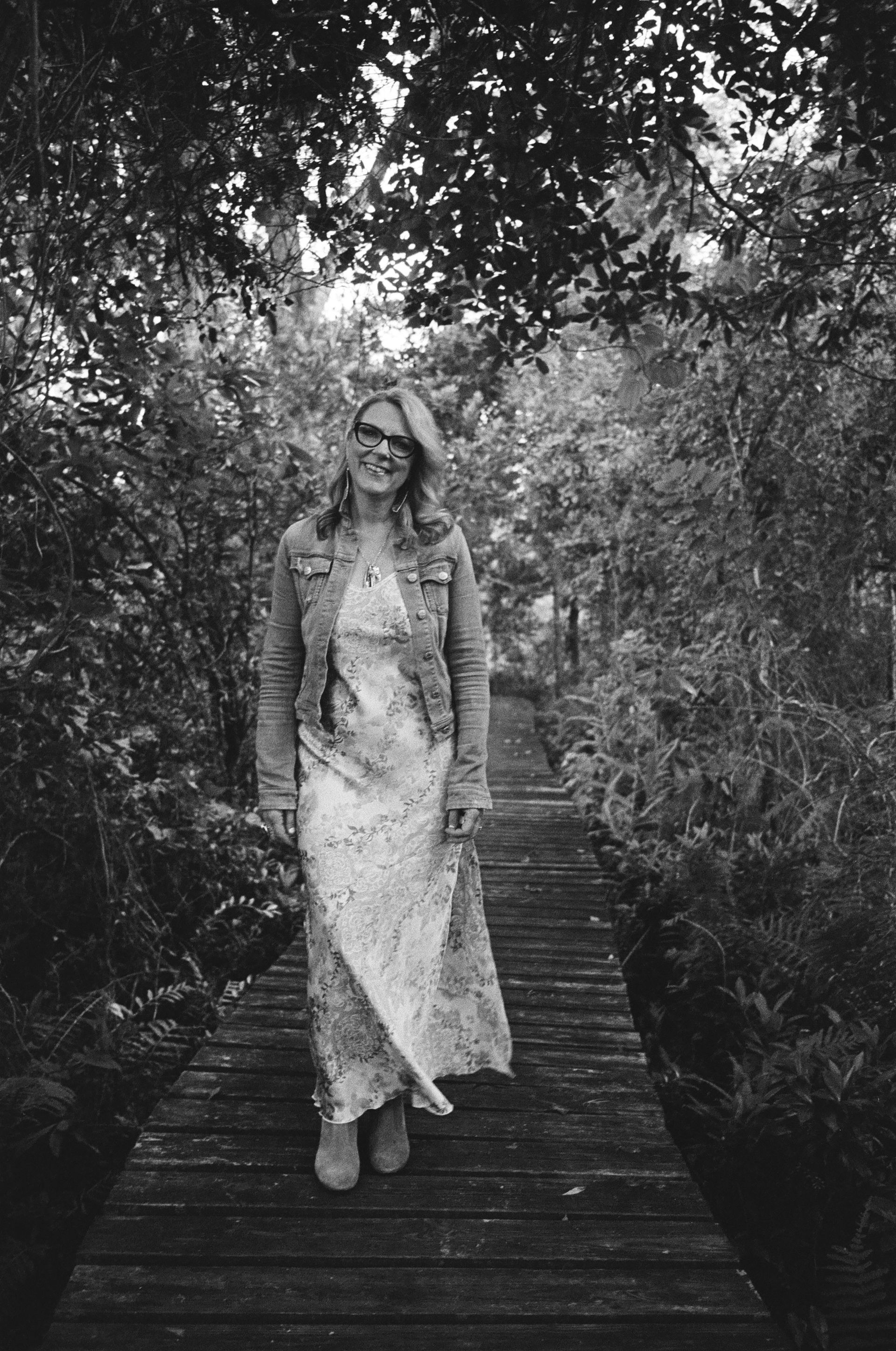 A woman in a long dress is standing on a wooden bridge in the woods.