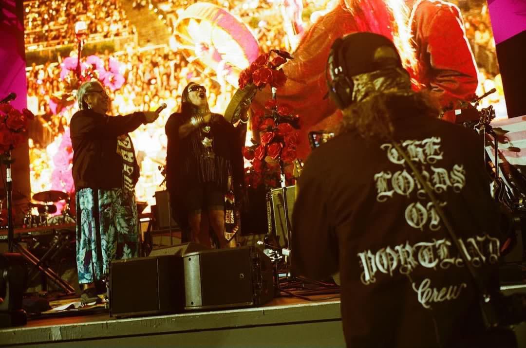 A man wearing headphones is standing on a stage watching a band perform.
