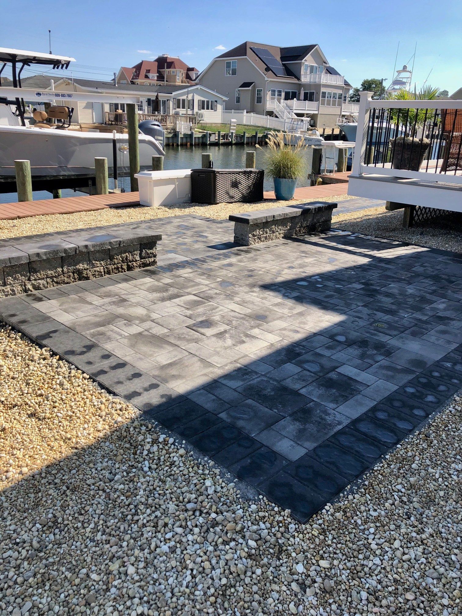 Brick patio near water with boat docks and houses. Gray pavers with gravel surround.