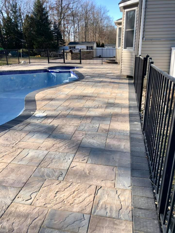 Poolside patio with textured pavers, black fence, and a pool.