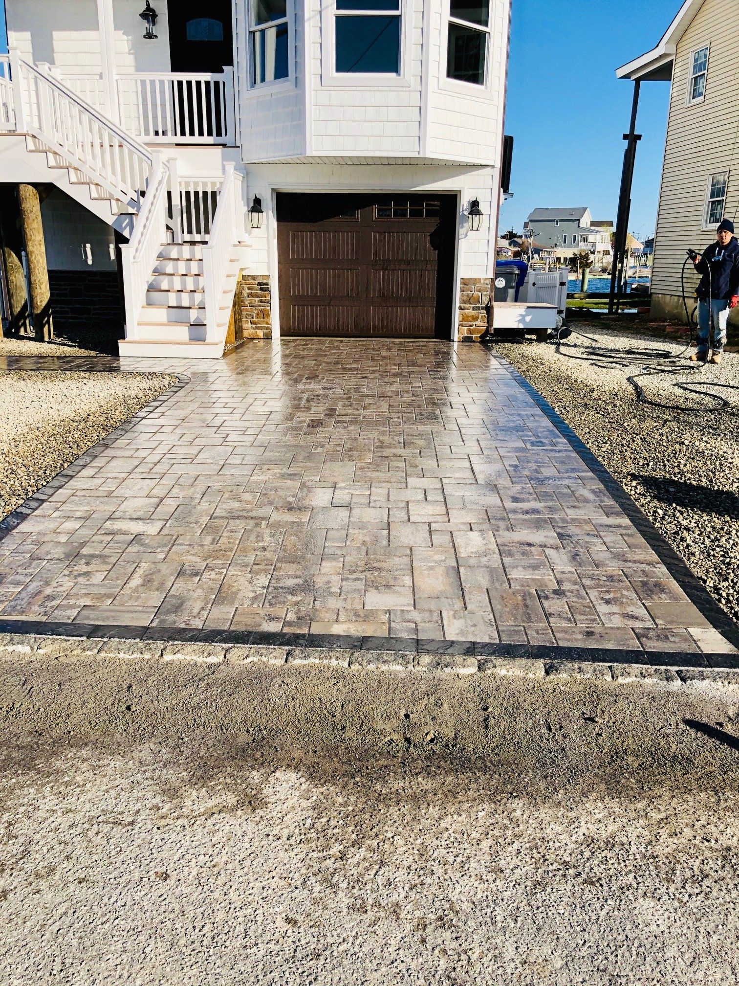 Newly paved brick driveway in front of a white house with a brown garage door.