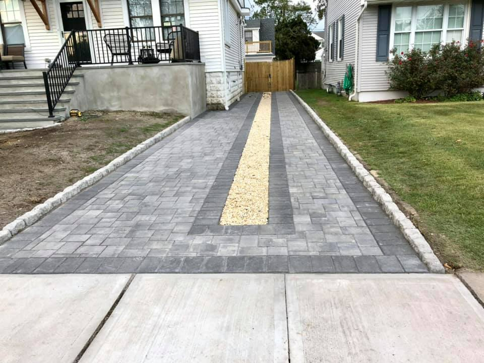 Paver driveway with gray and yellow brick design, bordered by concrete sidewalks and grass.
