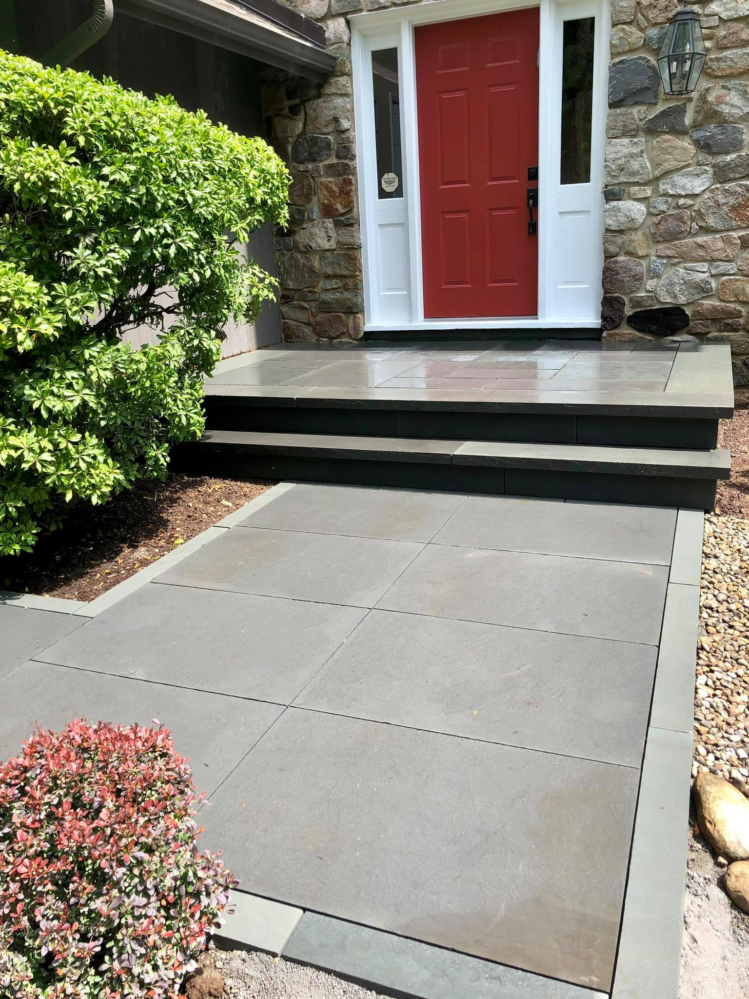 Stone steps leading to a red door with white trim. A paved walkway bordered by landscaping.