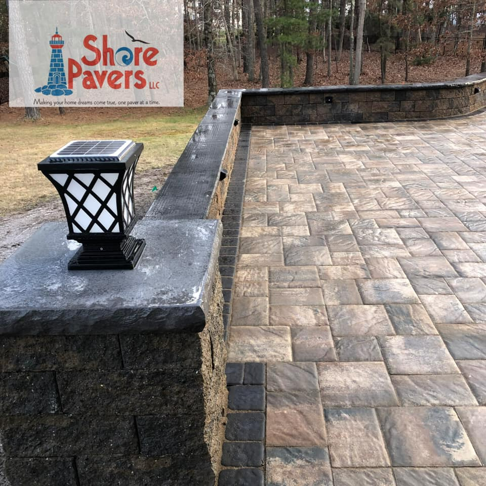 Paver patio with low retaining wall and solar lamp; dark pavers, stone wall, outdoor setting.