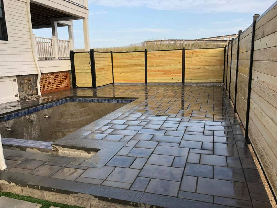 Backyard patio with pool, pavers, wooden fence. Cloudy sky, beige house.