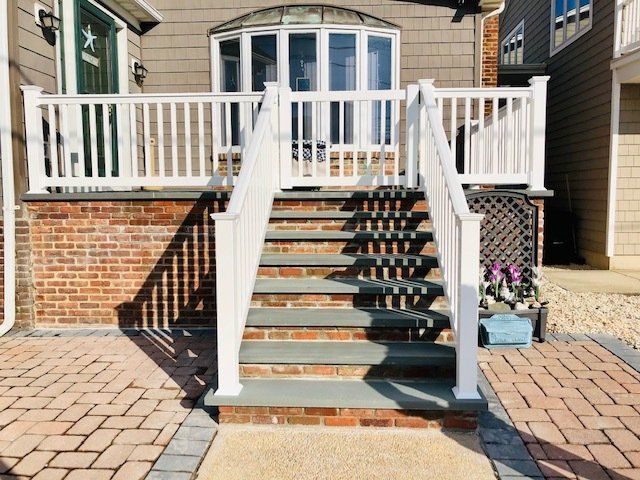 White staircase leading to a house with white railing, brick facade, and paved entrance.