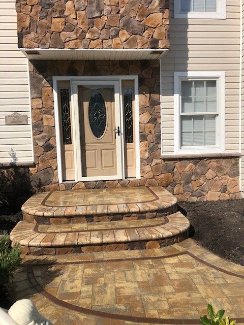 Beige house entrance with stone veneer, tan door, steps, and walkway.
