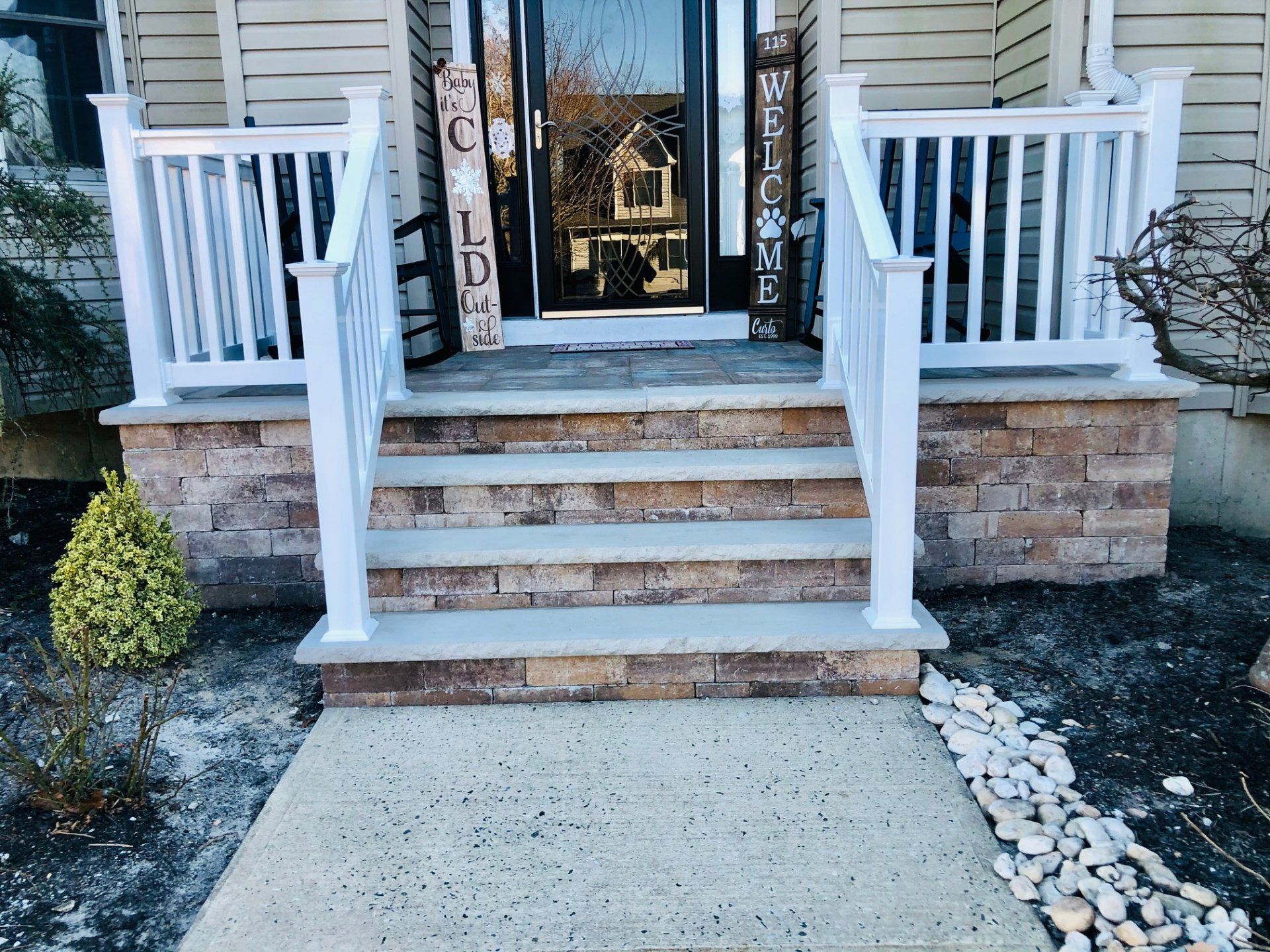 Front porch with brick facade, concrete steps, white railings, and a welcome sign.