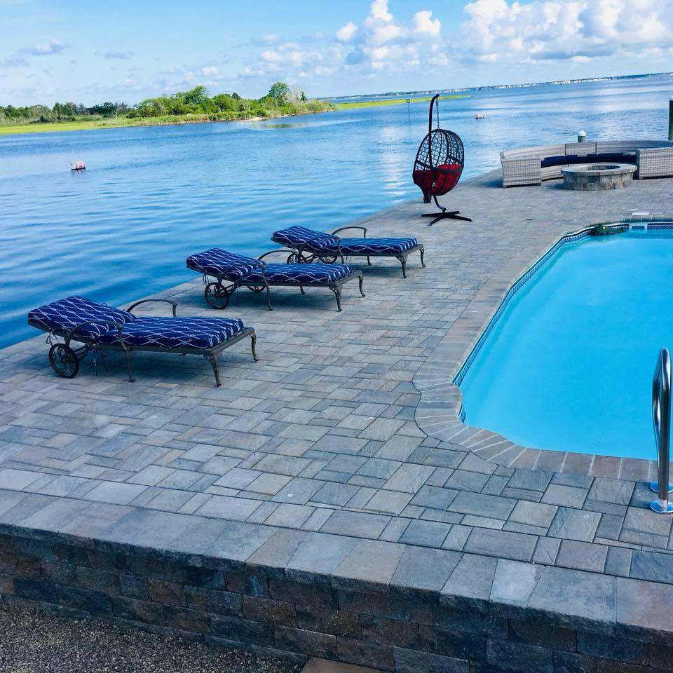 Poolside scene with blue water, lounge chairs, and a red hanging chair.