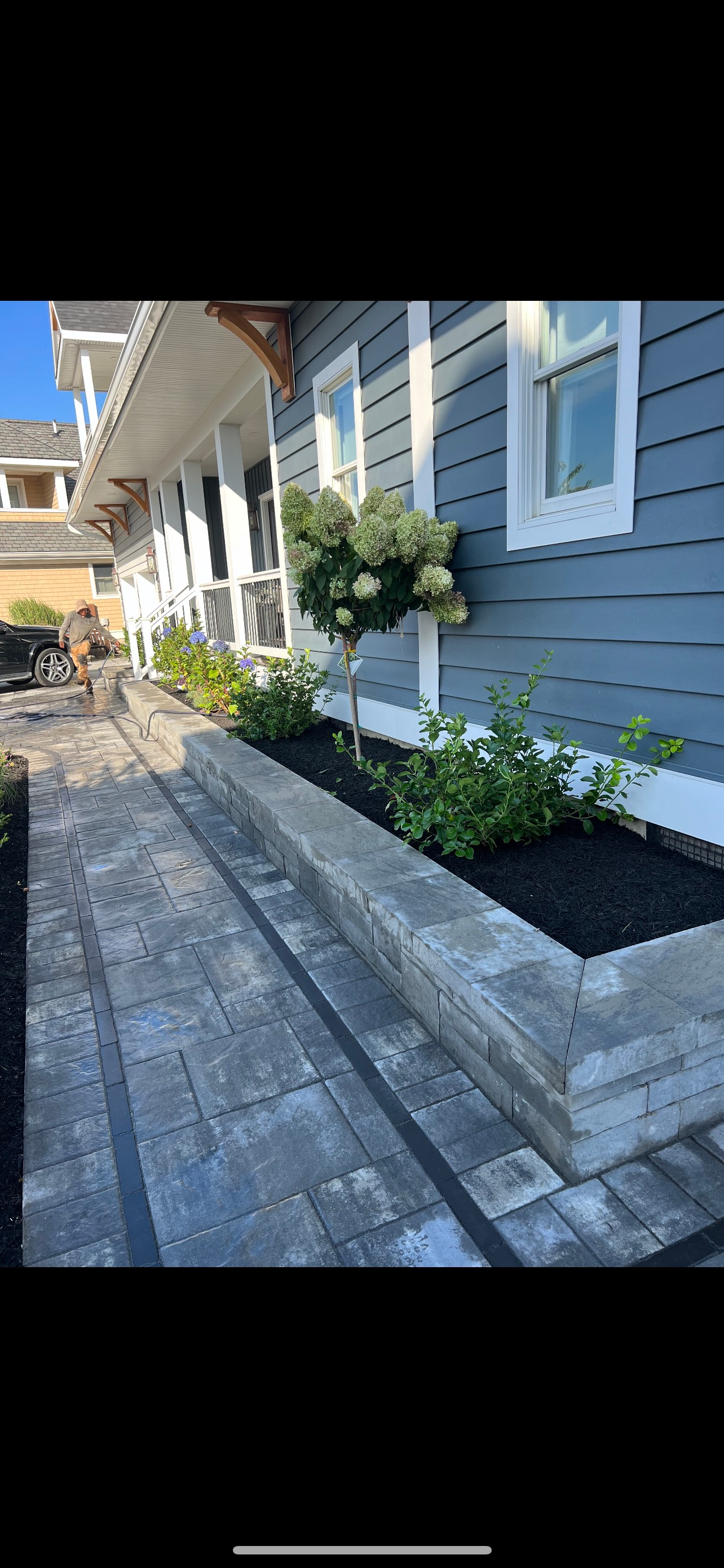 Gray brick pathway and raised garden bed beside a blue house with white trim.