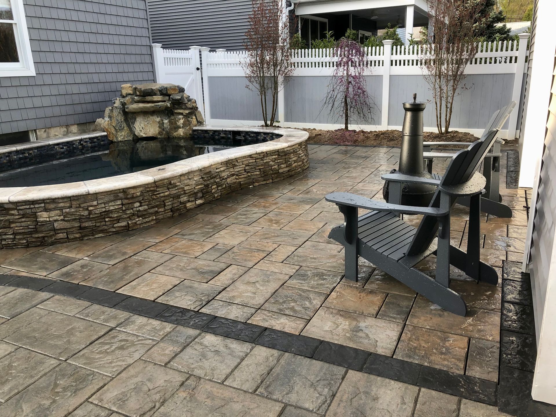 Patio with stone pavers, water feature, Adirondack chairs, and a fireplace.