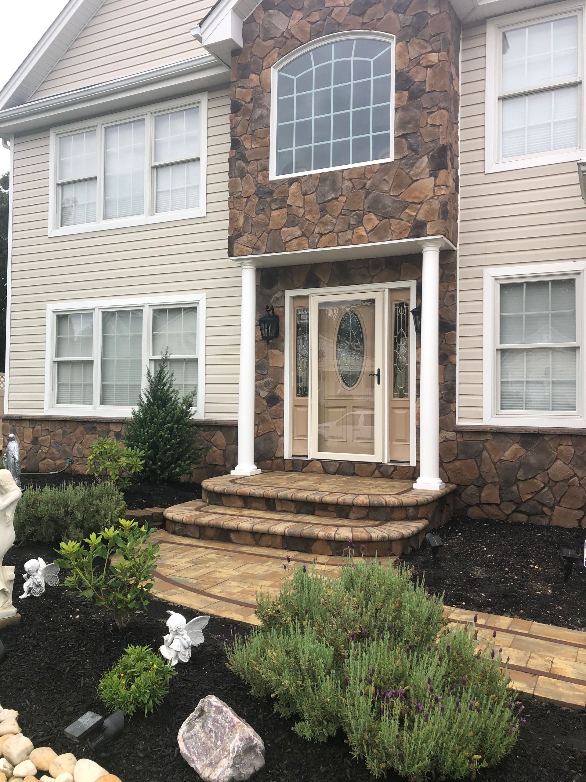 House exterior with stone facade around the entry, beige siding, a walkway, and manicured landscaping.